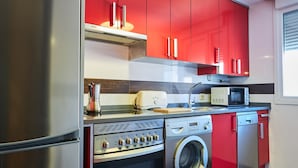 Une cuisine moderne dotée d’appareils électroménagers en acier inoxydable, de meubles de rangement rouges et d’un lave-linge encastré.