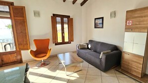 A room with a wooden cabinet, a grey sofa, an orange chair, a small table, and a window with blinds. - Playa 2 - 1 Habitaci N Vistas AL MAR (Villajoyosa)