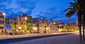 A coastal street lined with colorful buildings, palm trees, and a sandy beach.