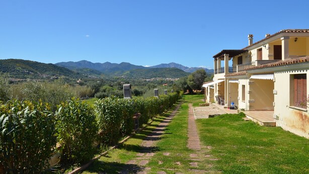 A villa with a paved pathway leading to a terrace, surrounded by lush greenery and a mountainous backdrop. - Fta-bel01 APT 6 PAX Vicino AL Mare (Budoni)