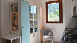 A kitchen with a built-in stove, a dining area with a table and a chair, and a cabinet with glass doors. - Fta-bel01 APT 6 PAX Vicino AL Mare (Budoni)
