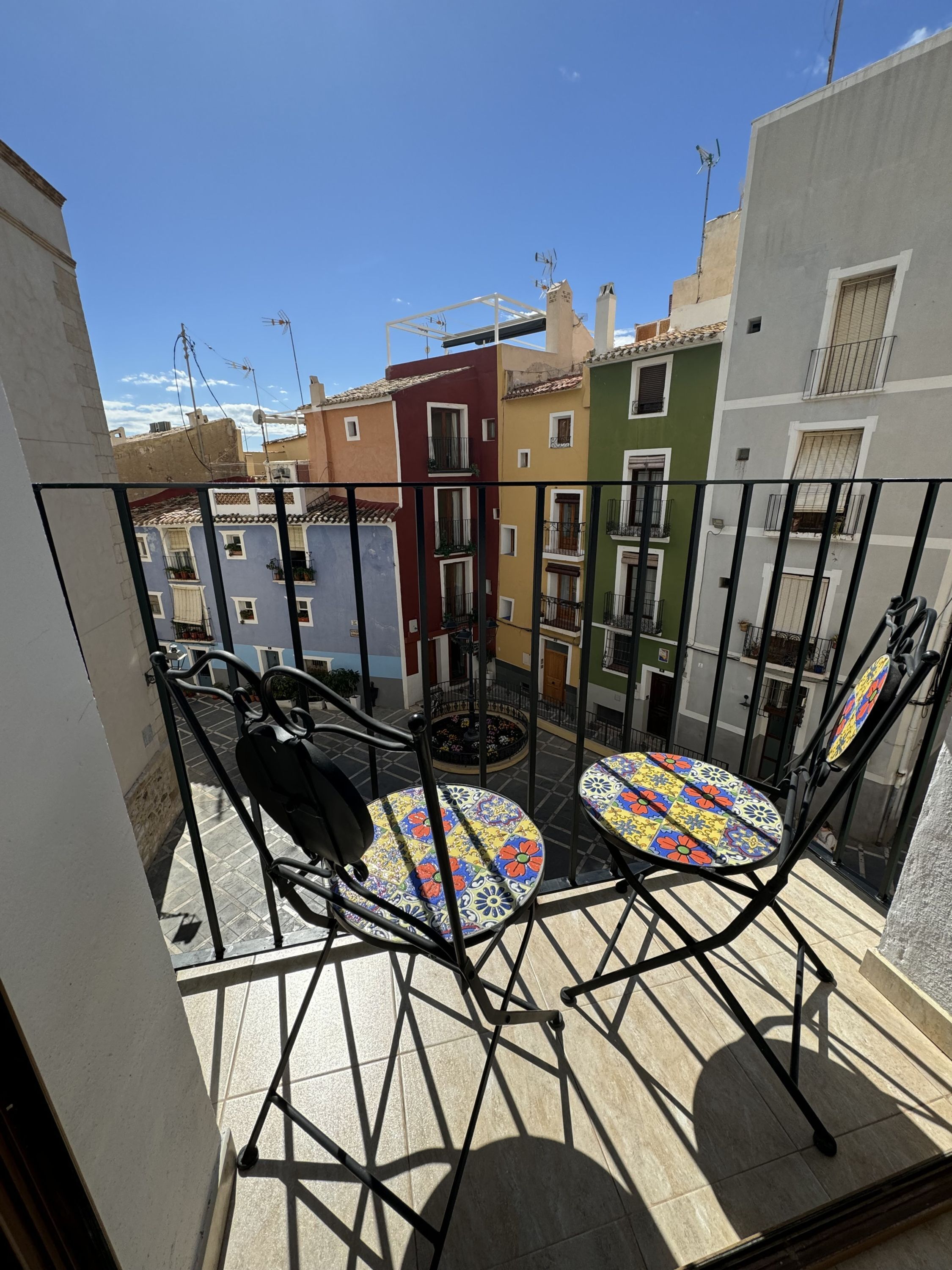 A balcony with two chairs and a small table, overlooking colorful buildings.