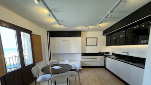 A compact kitchen with a dining area, a view of the sea through a large window, and a modern design with black and white cabinetry.