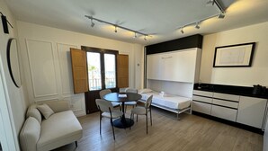 A compact hotel room with a bed, a small table, and chairs. There is a window with a view of the outdoors.
