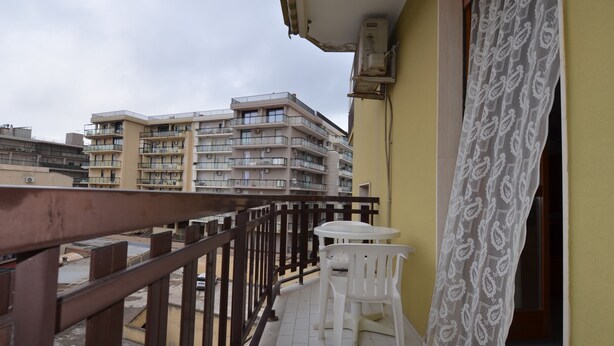 A balcony with a table and chairs, a patterned curtain, and a view of multi-story buildings.
