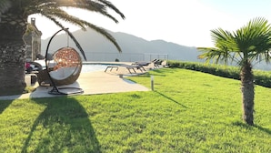A poolside area with a swing chair, lounge chairs, and a palm tree. - Villa d Exception vue mer Panoramique Piscine (Saint-Florent)