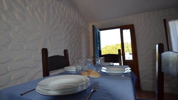 A dining table set with plates, glasses, and cutlery, with a view of greenery outside through a window. - Fpo-rose02p1 in Ottiolu (Budoni)