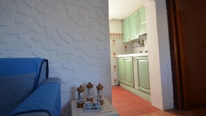 A room with a blue sofa, a small table with salt and pepper shakers, and a kitchen visible through an archway. - Fpo-rose02p1 in Ottiolu (Budoni)