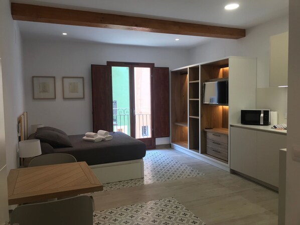 A bedroom with a bed, a bedside table, a desk, a chair, a wardrobe, and a television.