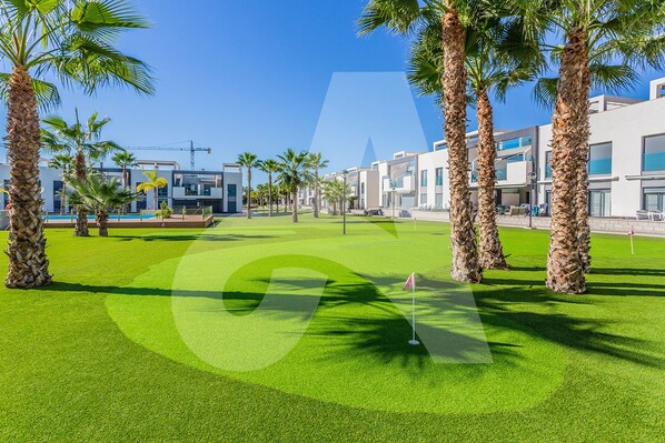 A golf course with palm trees and modern buildings in the background. - Casa Nicola in Guardamar (Guardamar del Segura)