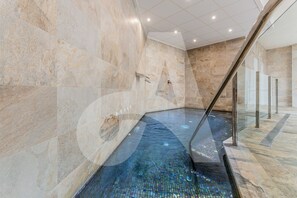 A modern indoor pool area with a clear glass floor, marble walls, and a glass railing. - Casa Nicola in Guardamar (Guardamar del Segura)
