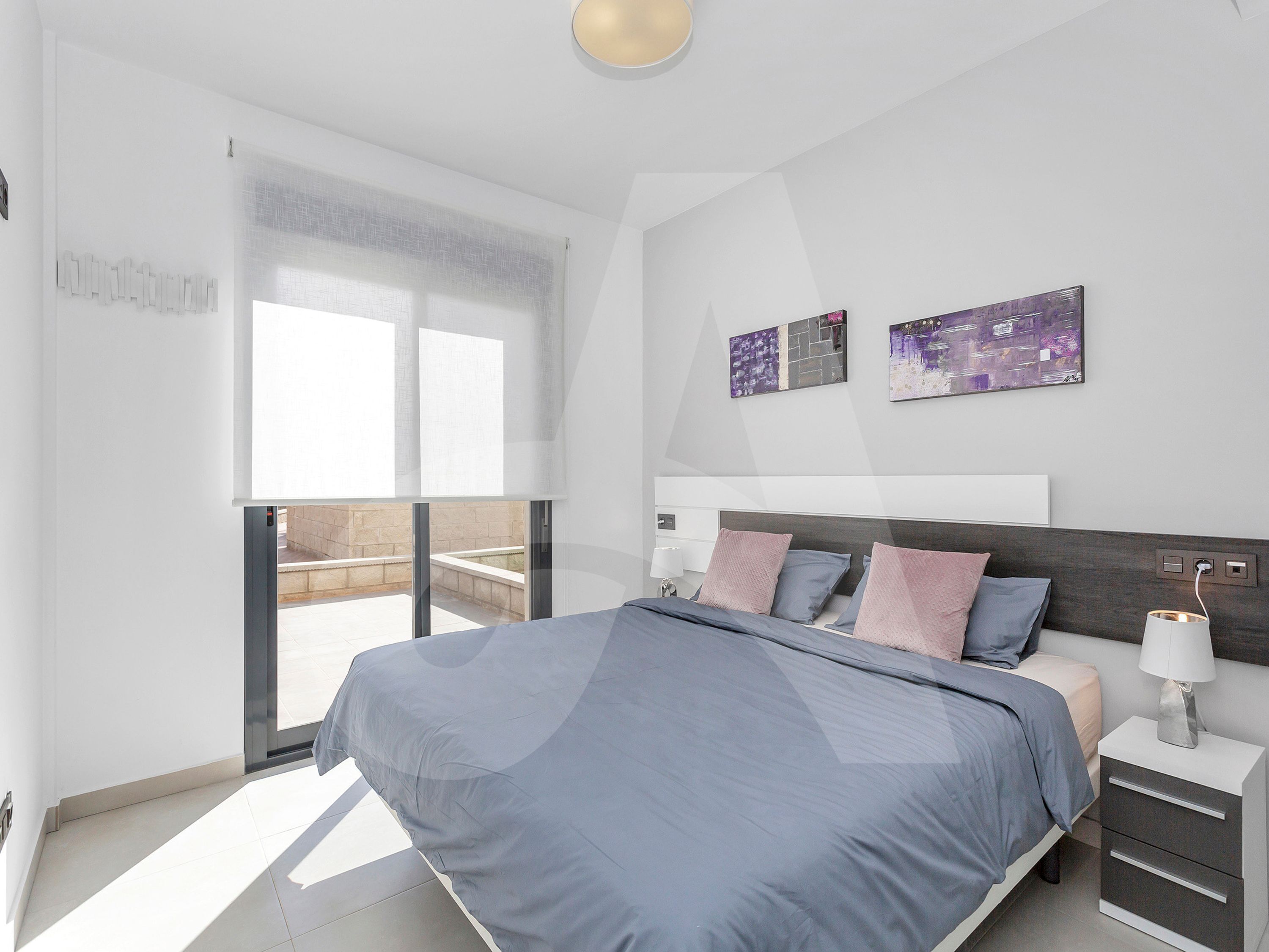 A modern bedroom with a large bed, a nightstand, a lamp, and two abstract wall art pieces.