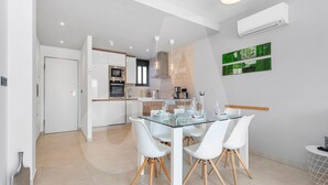 A modern kitchen with white cabinetry, a built-in oven, and a dining area with a glass table and white chairs. - Casa Nicola in Guardamar (Guardamar del Segura)
