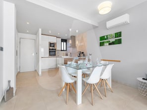 A modern kitchen with white cabinetry, a built-in oven, and a dining area with a glass table and white chairs. - Casa Nicola in Guardamar (Guardamar del Segura)