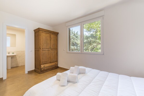 A bedroom with a large bed, a wooden wardrobe, a window with a view of trees, and a bathroom visible in the background. - VI El Cuartel 3 in Vila (Villatoro)