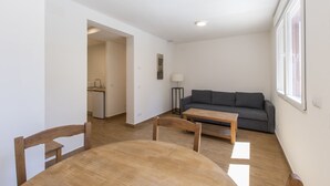 A modern living room with a grey sofa, wooden dining table, and chairs. A kitchen is visible in the background. - VI El Cuartel 2 in Vila (Villatoro)