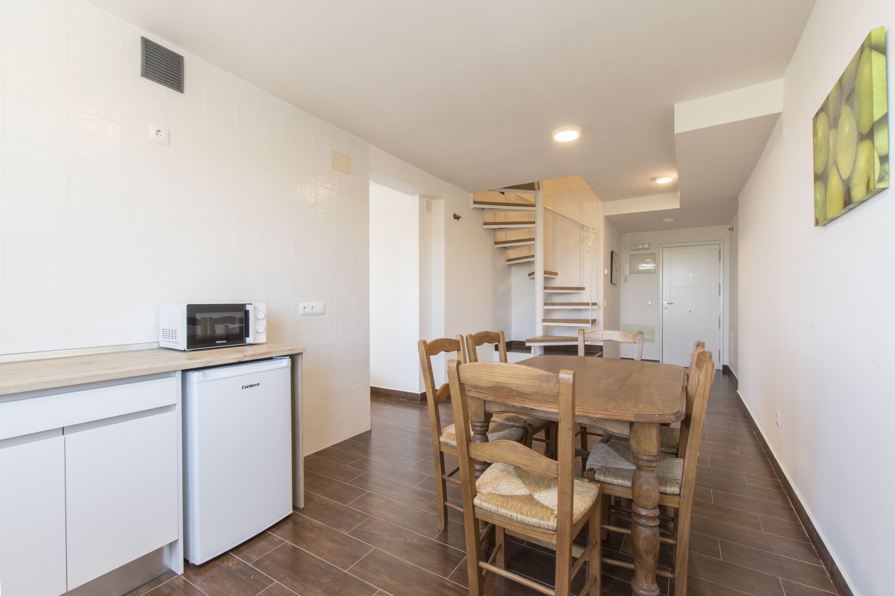 A compact kitchen with a microwave, a small refrigerator, and a dining area with a wooden table and chairs.
