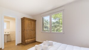 A bedroom with a large bed, a wooden wardrobe, a window with a view of trees, and a bathroom visible in the background. - VI El Cuartel 6 in Vila (Villatoro)