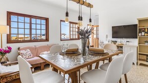 Een eetgedeelte met een houten tafel, witte stoelen en een televisie op de achtergrond.