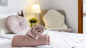 Een net opgemaakt bed met een opgerolde handdoek, een lamp en een plantje op een nachtkastje.