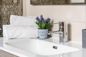 Et badeværelsesarrangement med vask, moderne armatur, et hvidt håndklæde og en potteplante med teksten "HOME & GARDEN".