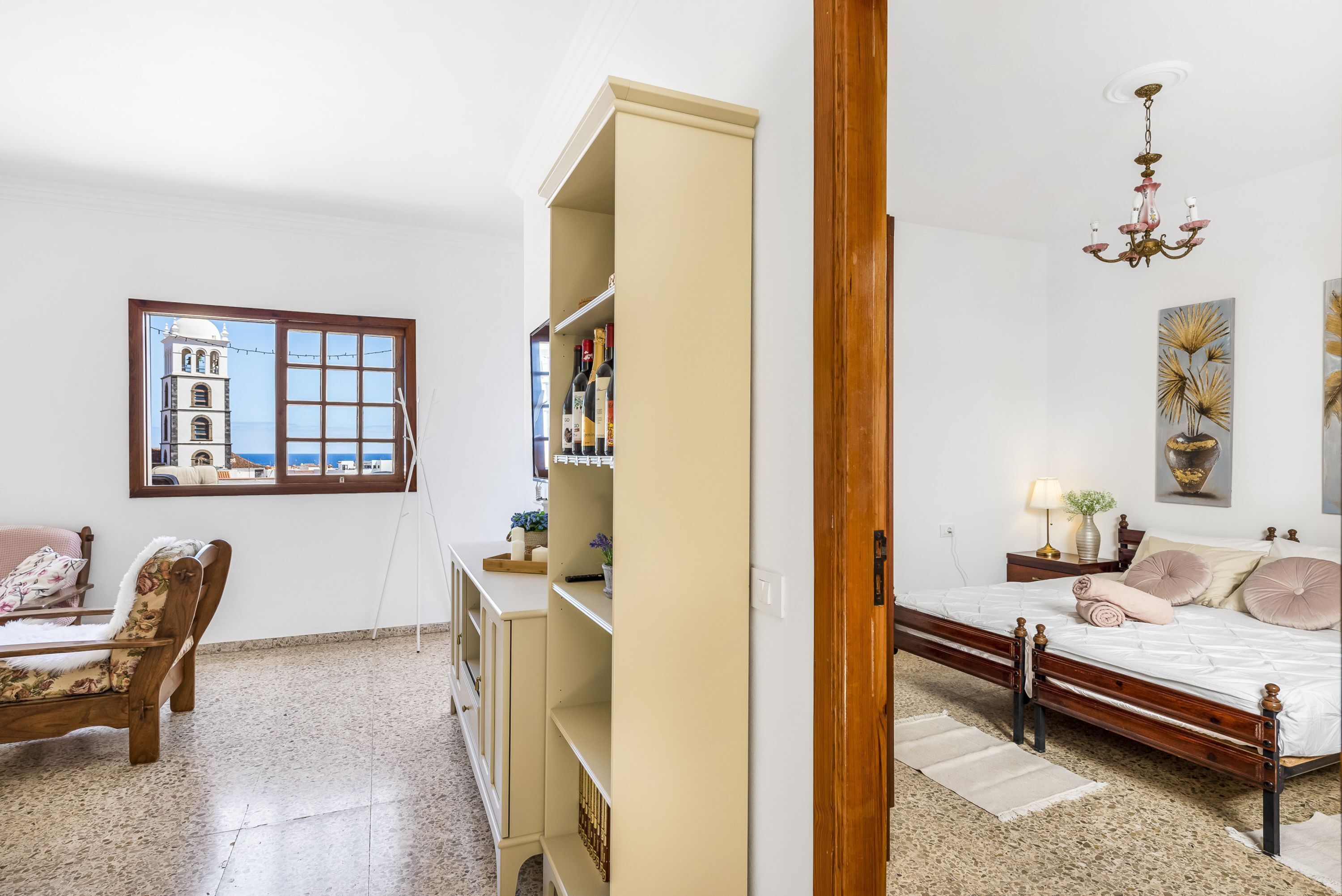 A bedroom with a bed, a desk, a chair, a wardrobe, and a window with a view of a bell tower.