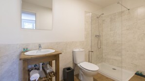 Een moderne badkamer met een houten wastafel, toilet, douche met glazen deur en een grote spiegel.