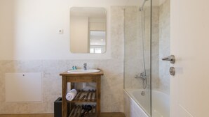 Une salle de bain équipée d’un lavabo, d’un miroir, d’une douche et d’une étagère en bois où sont posées des serviettes.