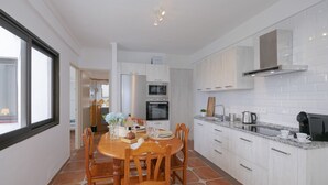 Een moderne keuken met witte kasten, een granieten aanrechtblad en een eethoek met houten stoelen en een tafel.