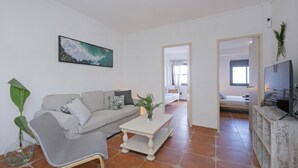 Een woonkamer met een grijze bank, een salontafel, een schilderij en een tv op een houten kast.