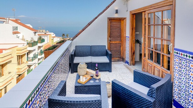 A balcony with blue wicker furniture, a wooden door, and a tiled wall. - Retreat w Ocean Views Private Parking Ensuite (Los Realejos)