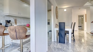 A modern kitchen with white cabinets, a marble countertop, and a dining area with a white table and black chairs. - Two-floor Penthouse w Complex Pool Outdoor Terrace (Arona)