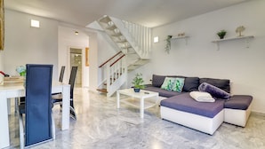 A modern living room with a white staircase, a grey sofa, a coffee table, and a dining area with a white table and chairs. - Two-floor Penthouse w Complex Pool Outdoor Terrace (Arona)