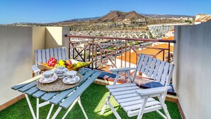 A balcony with a table set for tea, chairs, and a view of a mountain and town. - Two-floor Penthouse w Complex Pool Outdoor Terrace (Arona)