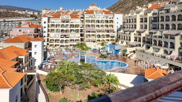 A hotel with multiple balconies, a swimming pool, and a landscaped area with palm trees. - Two-floor Penthouse w Complex Pool Outdoor Terrace (Arona)