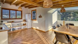 Eine geräumige Küche mit Holzbalken, einem Essbereich mit großem Tisch und Blick ins Grüne durch die Fenster.