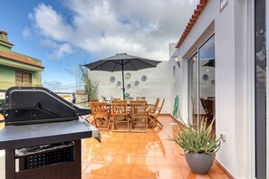 Un patio exterior con una parrilla, una mesa de comedor, sillas y una planta en maceta.