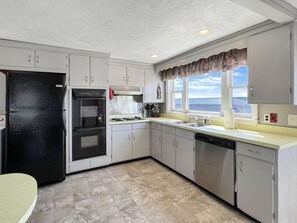 A kitchen with white cabinets, a black refrigerator, an oven, a dishwasher, and a window with a view of the sea. - Sweet Dreams W032 in Wells (Wells)