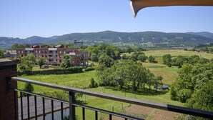 A balcony with a view of a green landscape, a brick building, and distant hills. - Great Escape by Fidalsa (Gautegiz Arteaga)