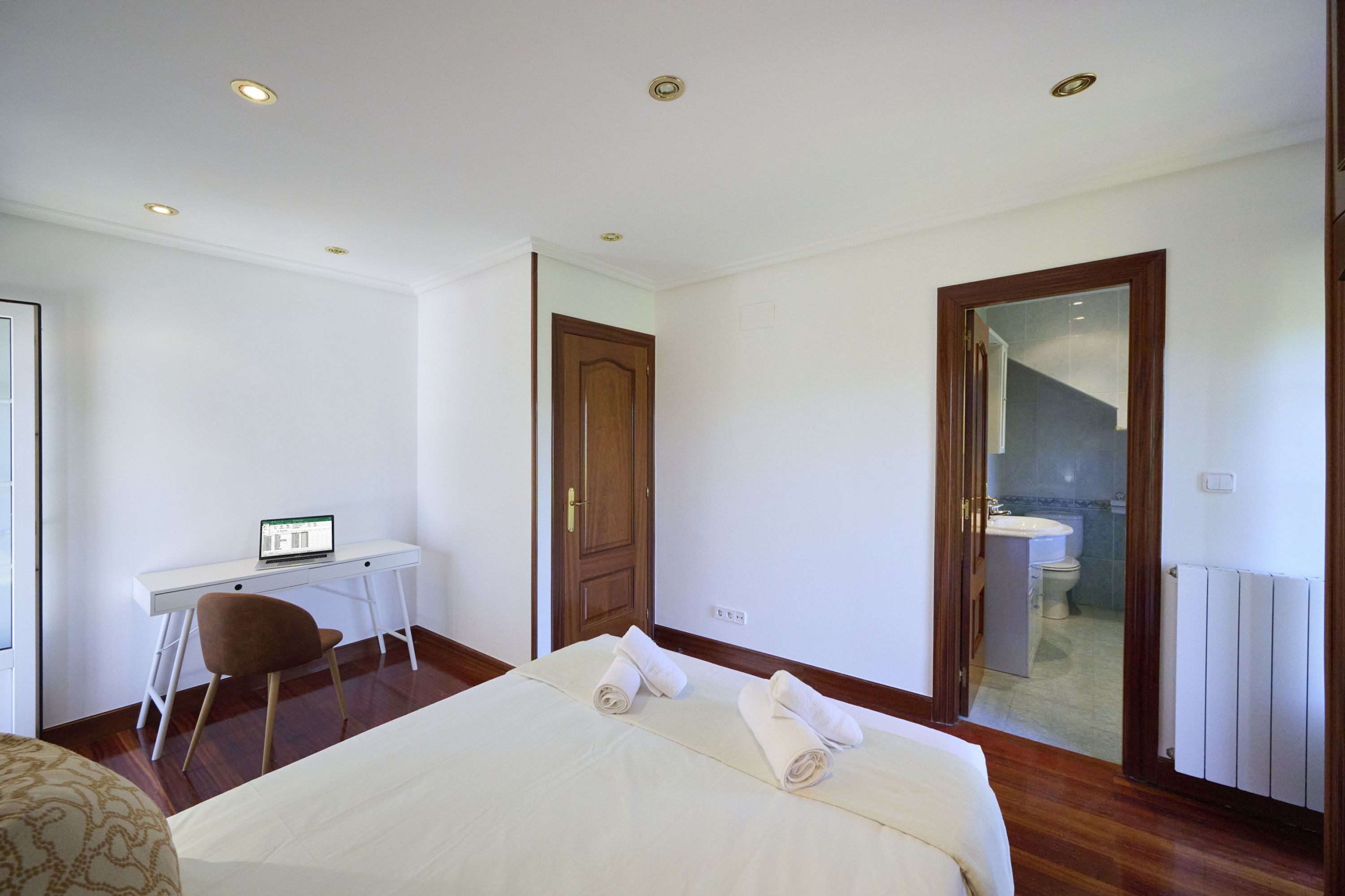 Ein Hotelzimmer mit einem Bett, einem Schreibtisch mit einem Laptop, einem Stuhl und einem durchgegangenen Türrahmen einsehbaren Badezimmer.