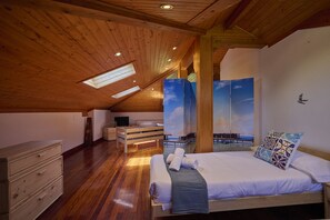 A bedroom with a wooden ceiling, skylight, a bed with white linens, a nightstand, a dresser, and a painting of a beach scene. - Great Escape by Fidalsa (Gautegiz Arteaga)