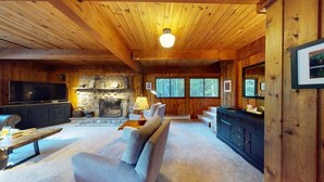 A cozy cabin interior with a stone fireplace, wooden walls, a television, and a comfortable seating area. - Treehouse Home in Ludlow (Ludlow)