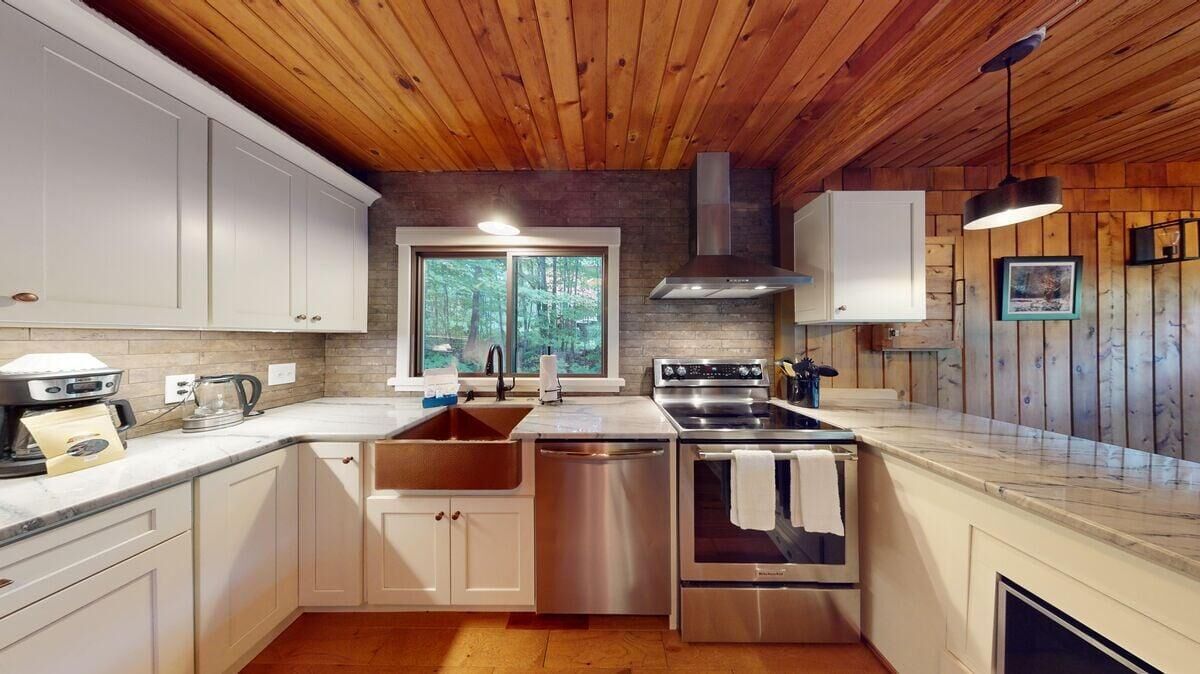 A modern kitchen with white cabinets, a large window, and stainless steel appliances.