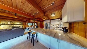 A spacious kitchen with a large island, wooden ceiling beams, and a stone accent wall. - Treehouse Home in Ludlow (Ludlow)