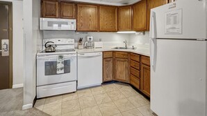 A compact kitchen with wooden cabinets, a white refrigerator, a microwave, an oven, and a dishwasher.