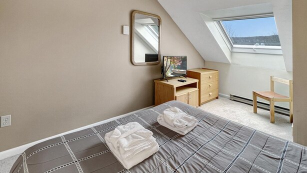 A bedroom with a bed, a desk, a chair, a mirror, and a window.