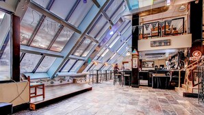A spacious interior with a high ceiling and skylights, a bar area with a counter and stools, and a seating area with tables and chairs.
