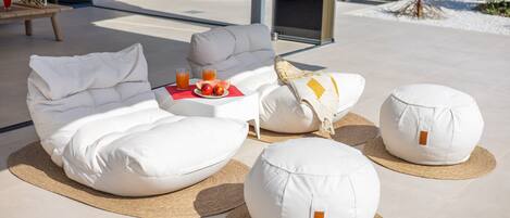 A modern outdoor seating area with a sofa, two bean bags, and a small table with drinks and fruit.