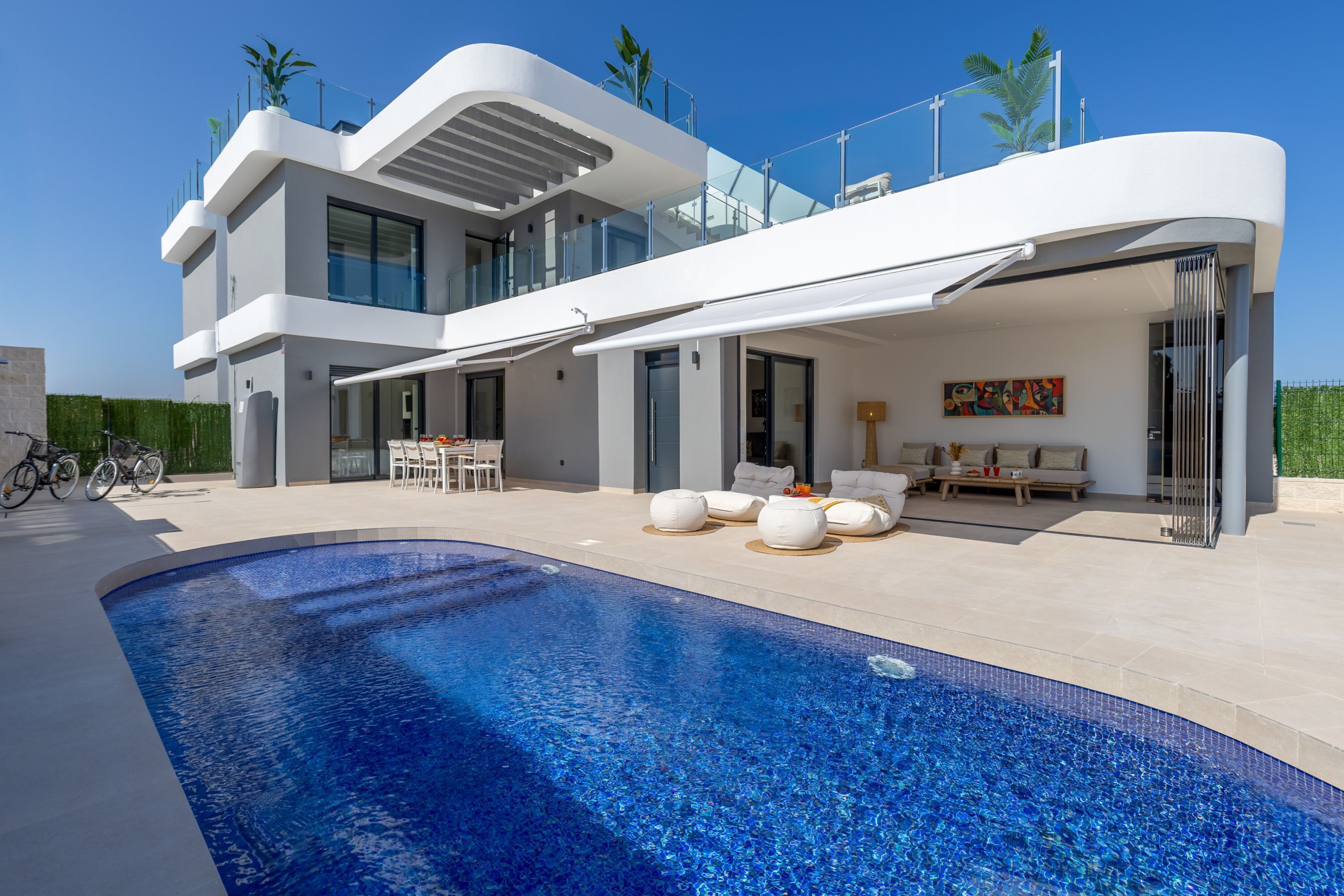 A modern two-story house with a swimming pool, outdoor seating, and a bike parked outside.