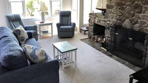 A living room with a stone fireplace, two grey armchairs, a blue sofa, and a small table with books. - Perkins Cove Gem - Q934 (Ogunquit)